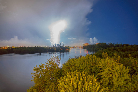 夜间长时间暴露的骡子闪电击中通过雷电风暴云在河岸城市灯的背景。 母质的电荷和功率