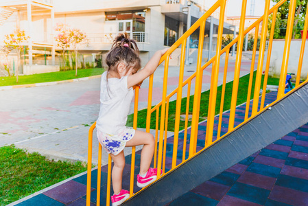 从操场上的金属楼梯栏杆上爬起来的可爱的小女孩的背面景色照片