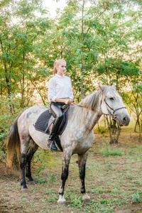 美丽的年轻姑娘，一头浅发，参加统一的比赛，微笑着，在秋天的日落中骑着一匹马