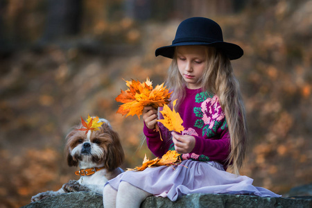 戴着帽子的可爱女孩编织着秋天枫叶的花环
