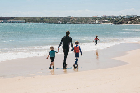 一个年轻的冲浪者和他的孩子们沿着海滩散步。联合消遣。一个幸福的家庭