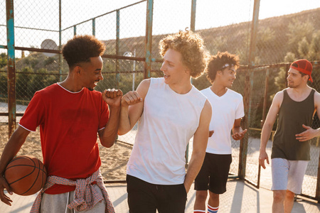 四个英俊的男孩在夏天阳光明媚的白天在操场上打篮球的肖像。