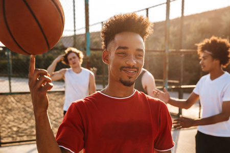 青少年运动员在户外操场上打篮球的肖像和美国人在手指上旋转球的肖像