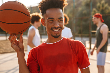 多民族男子在户外操场打篮球的照片和美国男子在手指上旋转球的照片