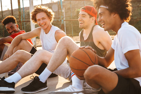 年轻快乐的篮球运动员坐在户外操场上，在夏日阳光明媚的日子里看比赛