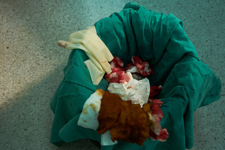 用染血的外科手套在绿色垃圾桶中测量缝线和纸张,以处理生物危害照片
