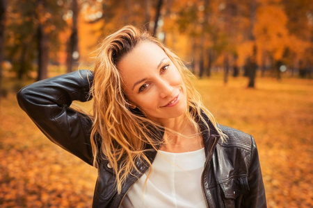 那个女孩走过秋天的公园。 在森林里穿着皮夹克的黑发。 黄叶落下。