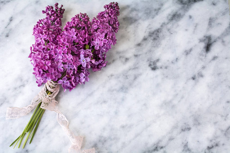 美丽的紫色丁香花，白色大理石背景上有粉红色的丝带。 顶部视图，复制空间