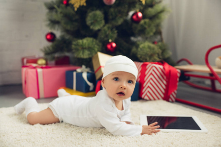 可爱的小宝宝，平板电脑躺在地板上，圣诞礼物和背景上模糊的树