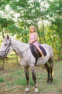 一个小可爱的女孩，戴着草帽，在阳光明媚温暖的秋日日落时骑马