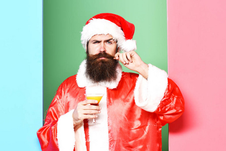长长的胡须，在圣诞节或圣诞毛衣和多彩工作室背景新年帽子举杯子，含酒精的饮料的严重脸上胡子的圣诞老人英俊