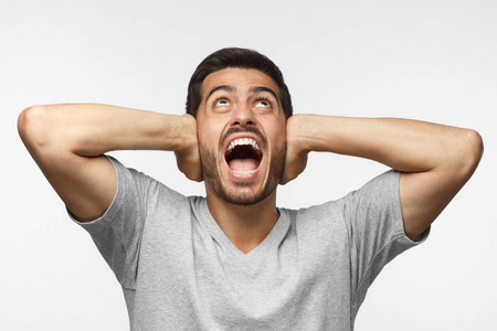 年轻人一边大声喊叫,一边抬头,一边紧张,用双手合耳照片