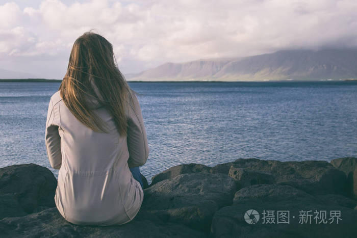 女人坐在雷克雅未克的海岸线上看着大海.