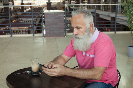 在咖啡店的智能手机上连接着成熟的胡子男人