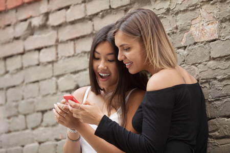 两个快乐的女性朋友在公园的户外用智能手机分享社交媒体