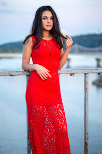 美丽的女孩穿着红色的礼服, 在一座旧篱笆附近的桥上摆姿势