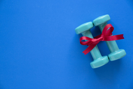 两个绿色哑铃与红色礼品弓在蓝桌背景运动和健康的概念
