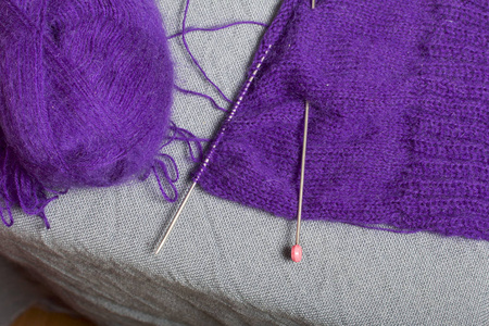 用钢编织针编织。 一团紫色的线和钢编织针在一个未完成的针织。