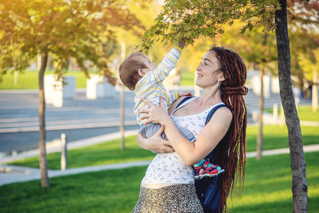 年轻的现代幸福妈妈和小儿子在阳光公园散步。 母亲的喜悦和秋天心情的概念