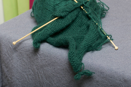用木制针织编织。 一团深绿色的线和木制针织针在一个未完成的针织。