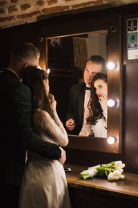 这对年轻的新婚夫妇站在拥抱中，在室内照镜子