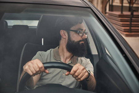 一个年轻迷人的男人驾驶着一辆车，看着透过挡风玻璃看到的风景。 小心的司机把手放在方向盘上看着路。