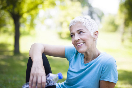 微笑的老年妇女坐在草地上锻炼后放松的肖像