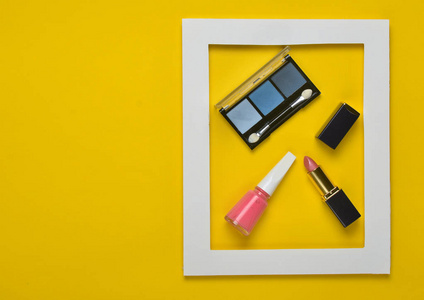 黄色背景上白色框架中的女性化妆品。 阴影弥补口红指甲油。 极简主义趋势。 上面的风景。 复制空间