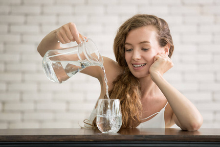 在房间里，一个年轻的女人把水壶里的水倒进玻璃杯里