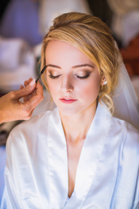 年轻美丽的新娘的肖像，她闭着眼睛坐着，化妆师画眉毛。