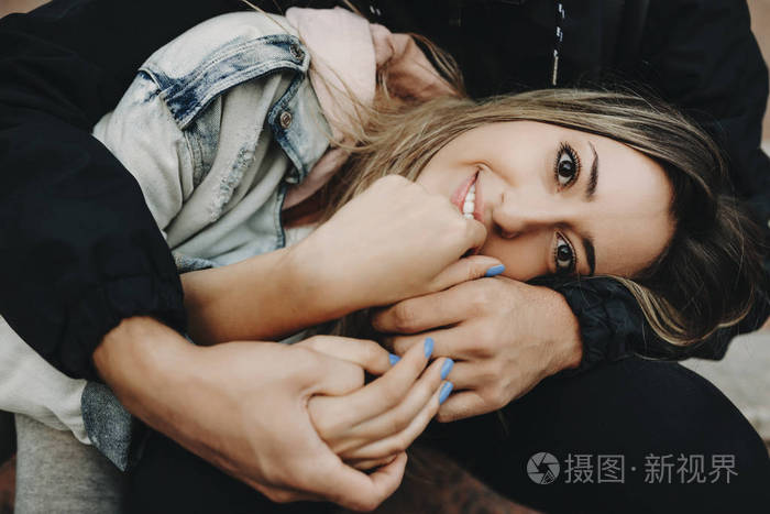 年轻的金发女子抱着一个矮个子男人坐在台阶上对着镜头微笑