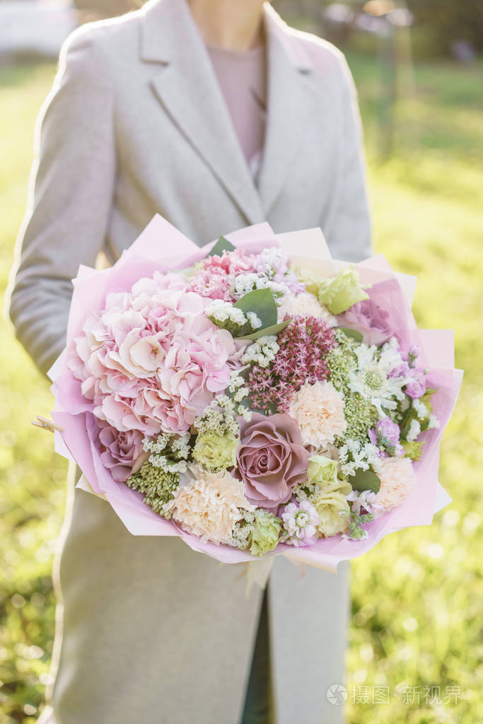 年轻女孩捧着一束美丽的春天花束插花与花绣球和花园玫瑰颜色浅粉色