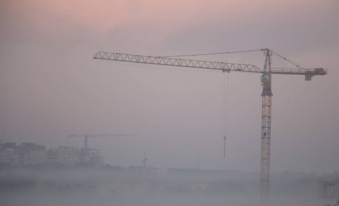 很高的建筑起重机在晨雾的灰色天空背景下关闭