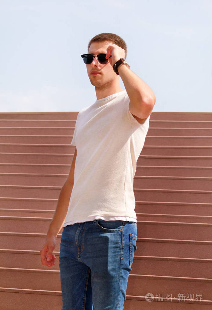 一个人独自站在楼梯上. 英俊的男孩带着太阳镜看手表.