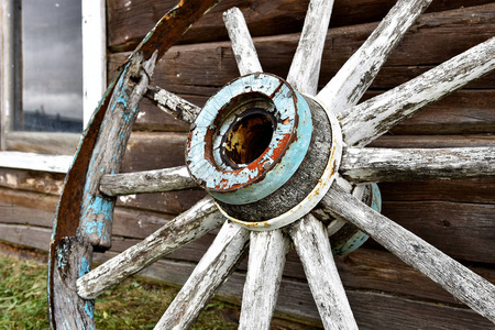 一个靠近的图像，一个旧的木车轮靠在一个木屋的侧面。