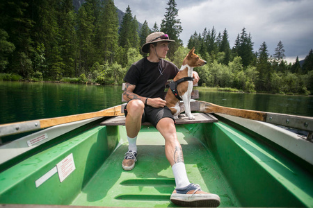 徒步旅行野营装备的年轻人和他的小狗宠物巴森吉犬一起坐在划艇上游泳高山湖泊享受健康活跃的生活方式