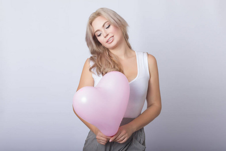 幸福的金发美女，手里拿着粉红色的心脏气球，手里拿着灰色的背景