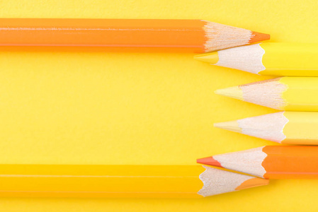 几支黄色和橙色的削尖铅笔在纸背景上的宏观照片