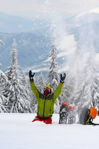 快乐的冒险家坐在冬天旅行的设备旁边，在覆盖着雪的巨大松树的背景下，在冬天去山上旅行时，把雪洒在自己身上。