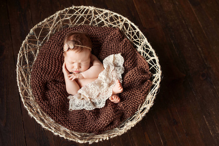 可爱的新生婴儿睡在篮子里。深棕色背景。