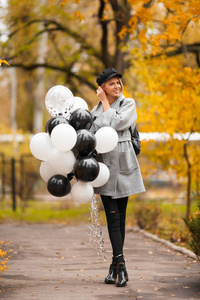 秋天的女人带着气球在秋天的公园里。穿灰色外套的时尚女孩
