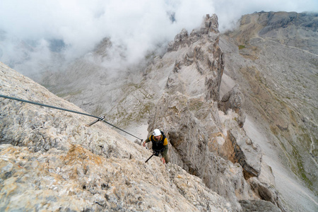 年轻英俊的男性登山者，在陡峭和裸露的岩石表面攀登阿尔塔巴迪亚在南蒂罗尔的经费拉塔。