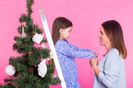 圣诞节的年轻妈妈和她的女儿在粉红色的背景圣诞树