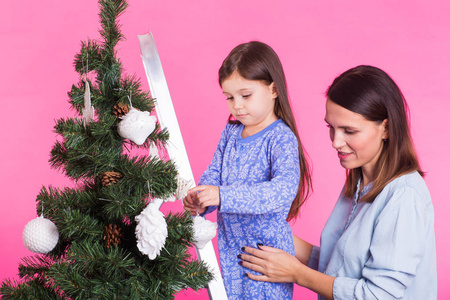 圣诞节, 童年和人的概念女孩站在阶梯梯子上装饰圣诞树与她的母亲在粉红色的背景