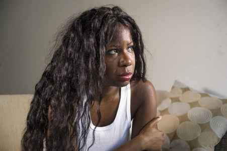 年轻有魅力和悲伤的黑人非裔美国妇女坐在沮丧的家里沙发上，感到焦虑和沮丧，患有抑郁焦虑危机或心碎