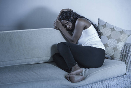 年轻有魅力和悲伤的黑人非裔美国妇女坐在沮丧的家里沙发上，感到焦虑和绝望，患有抑郁焦虑危机或心碎