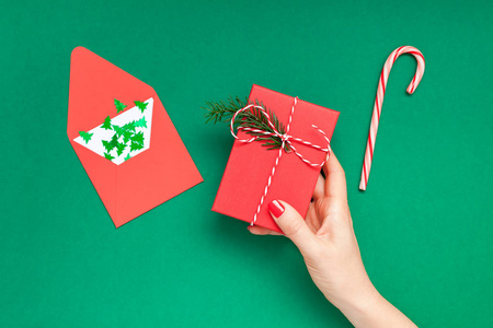 新年或圣诞节顶部查看圣诞节节日庆祝妇女手红指甲持有礼物盒复制空间绿色彩色纸背景。 模板贺卡