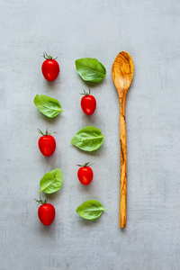 创意布局由木制勺子樱桃番茄和罗勒叶在浅色背景。 健康的烹饪原料。 食物概念。 平躺式顶部视图
