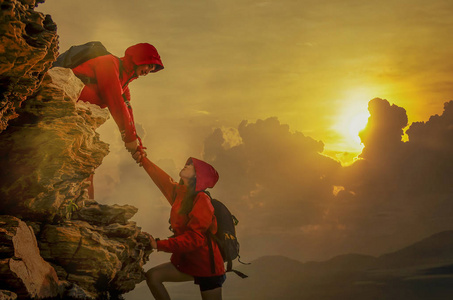 困难人员雄性和雌性远足者爬上山崖,其中一人伸出援手.