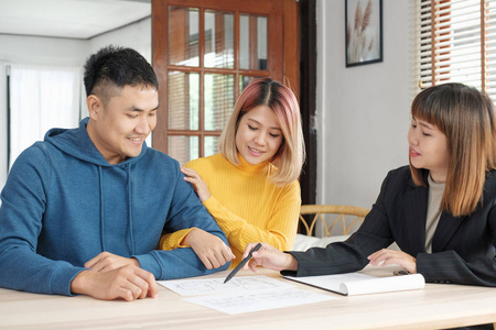 亚洲夫妇听房地产经纪人解释房屋计划和房屋合同在桌子上。购买新公寓房地产